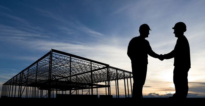 Two men shaking hands in front of construction site at sunset