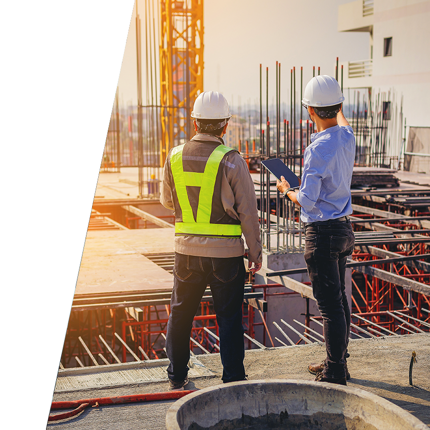 Two construction workers viewing top floor of commercial construction project while comparing plans on tablet to what is completed on job site.