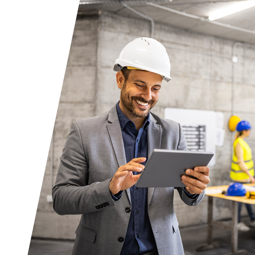 Risk manager wearing gray suit and blue button down shirt smiling at his tablet while standing in construction site.