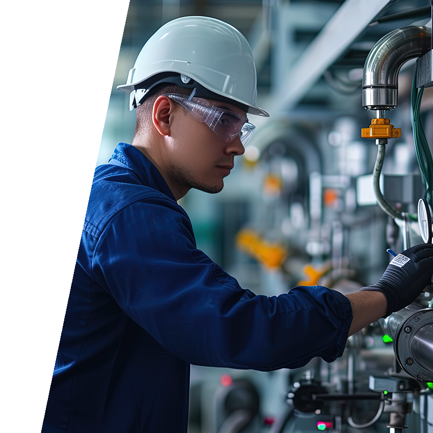 Man wearing blue work jacket, safety glasses, and white hard hat evaluating water pipes and valves.